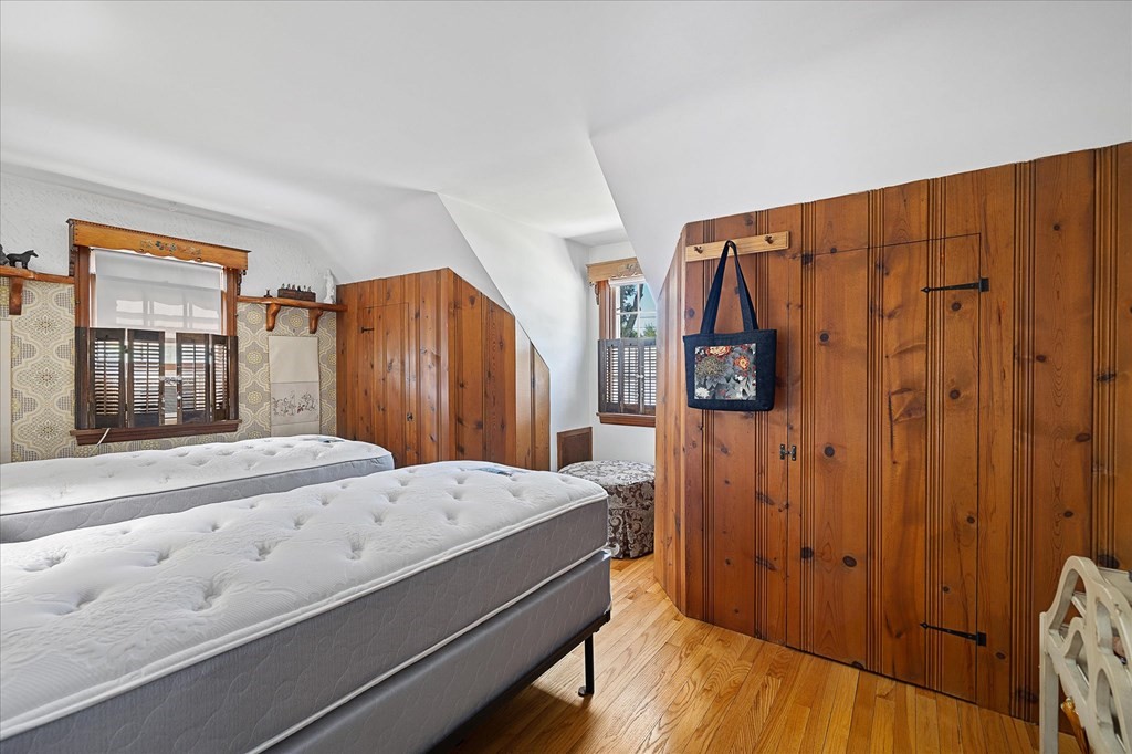 Bedroom with two white mattresses, wood-paneled walls, built-in wardrobes, and hardwood flooring.