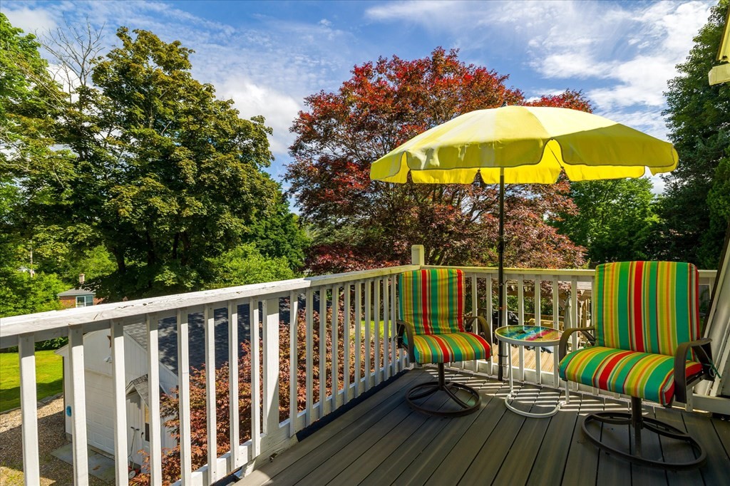 Deck with striped patio chairs and a yellow umbrella overlooking mature trees.