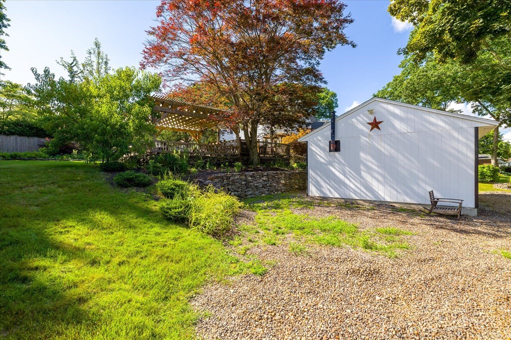 Gravel-and-grass yard with a white shed, pergola, and autumn tree.