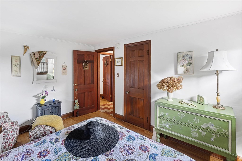 Bedroom with a patterned bedspread, black woven hat, pale green dresser, and dark wood doors.