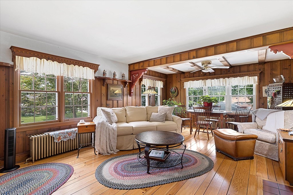 Living room with wood paneling, hardwood floors, large windows, and a dining area.