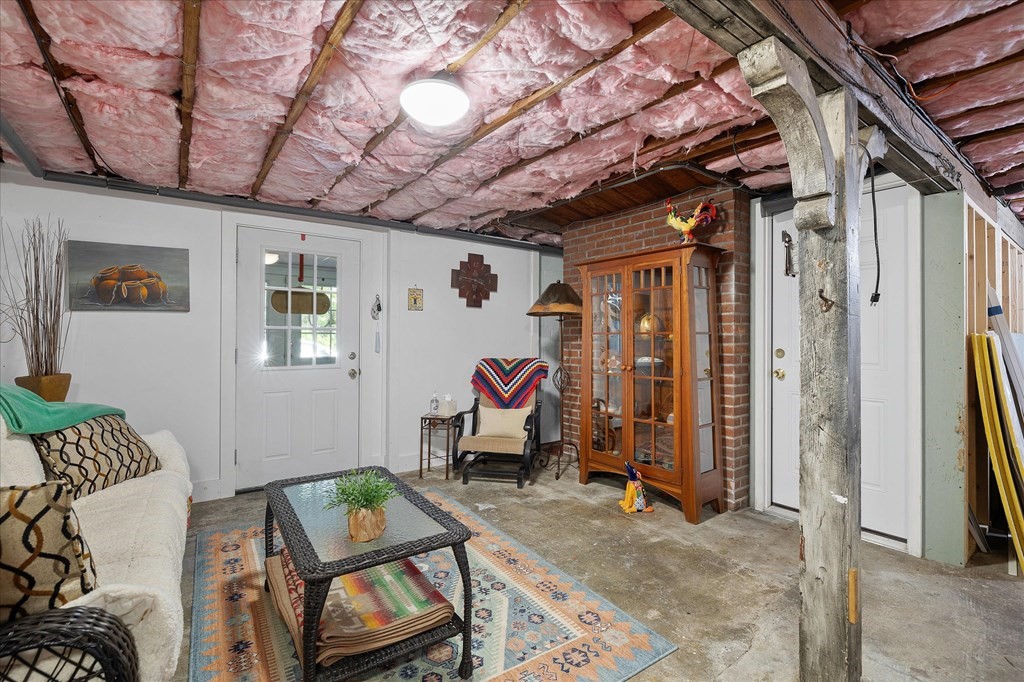 Basement sitting area with exposed insulated ceiling, concrete floor, sofa, and brick wall.