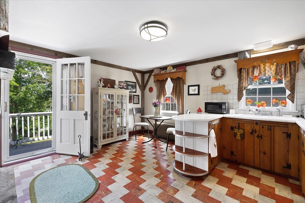 Kitchen with warm wood cabinets, a white island, patterned tile floor, and an open door to a tree-lined deck.