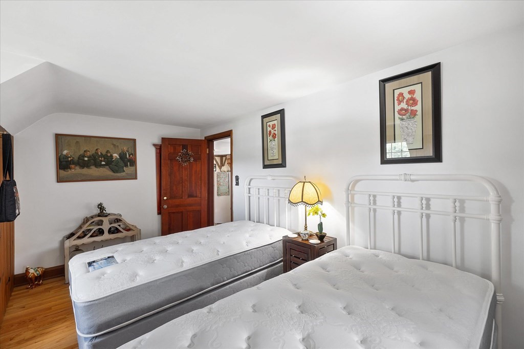 Bedroom with two white metal beds, a wooden nightstand, and framed floral artwork.