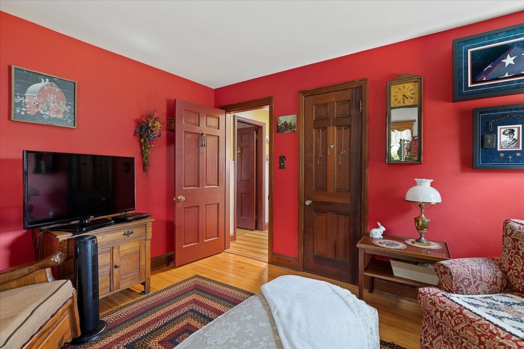 Bedroom with vivid red walls, wooden dresser and television, patterned rug, and bed in the foreground.
