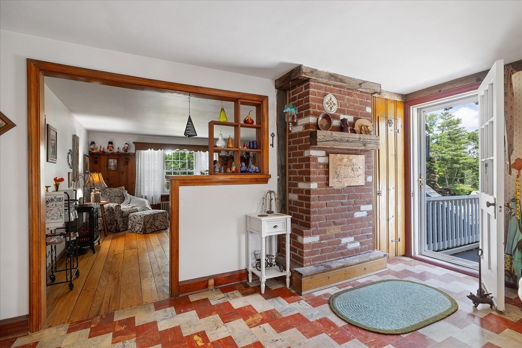 Interior with a brick fireplace, patterned tile floor, and open door to a porch.