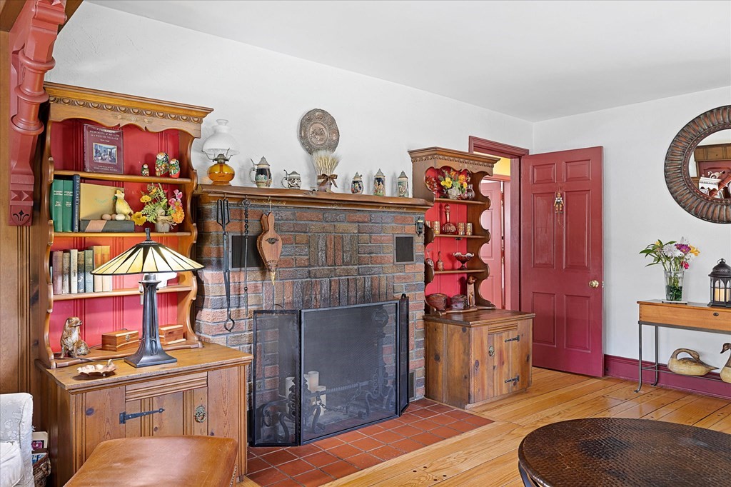 Living room with a brick fireplace, ornate built-in shelves, red trim, and hardwood floors.