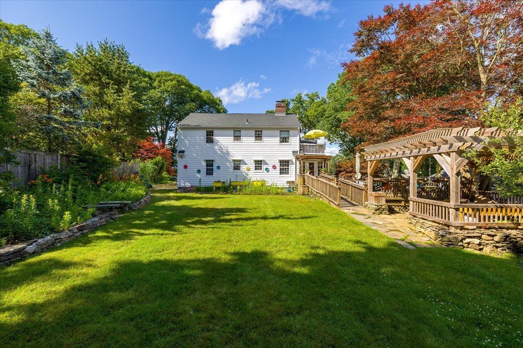 White two-story house overlooking a broad lawn, with a raised deck and wooden pergola.