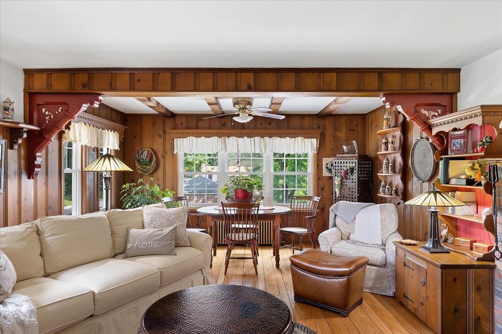 Wood-paneled living room with a beige sectional, armchairs, and large windows overlooking greenery.