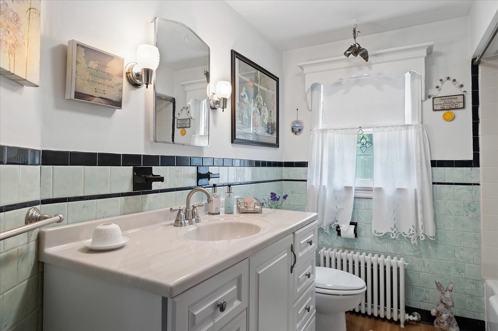 Bathroom with a white vanity, mint-green tiled walls, and a curtained window.