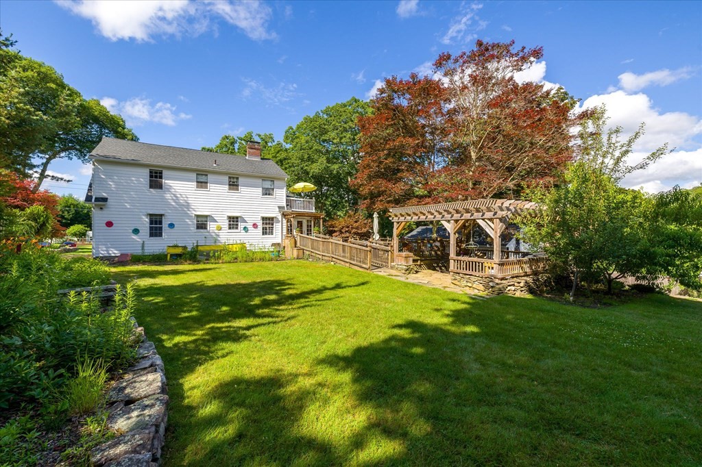 White two-story home overlooking a broad lawn, raised deck, and pergola-covered patio.