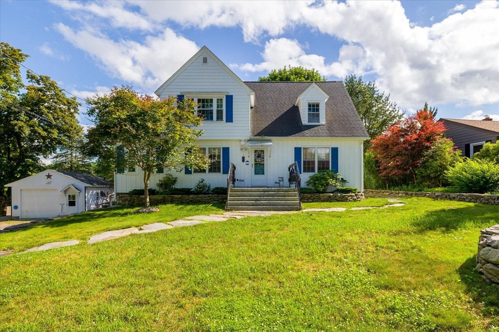 White two-story home with blue shutters, front steps, and a detached garage beside a broad lawn.