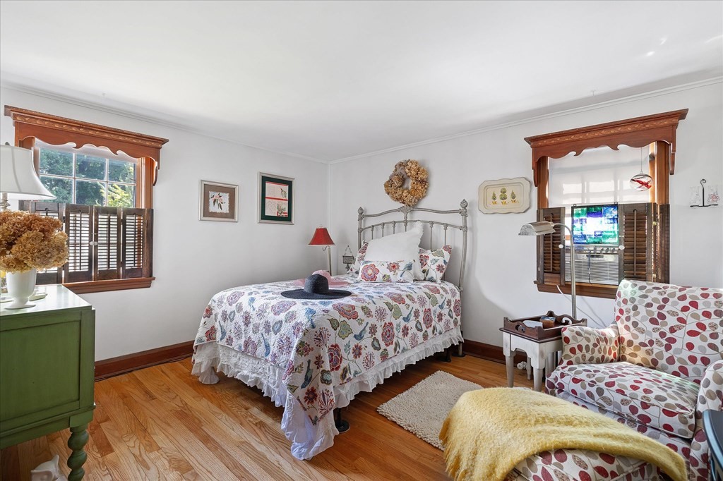 Bedroom with a floral-quilted bed, hardwood floors, and carved wood window trim.
