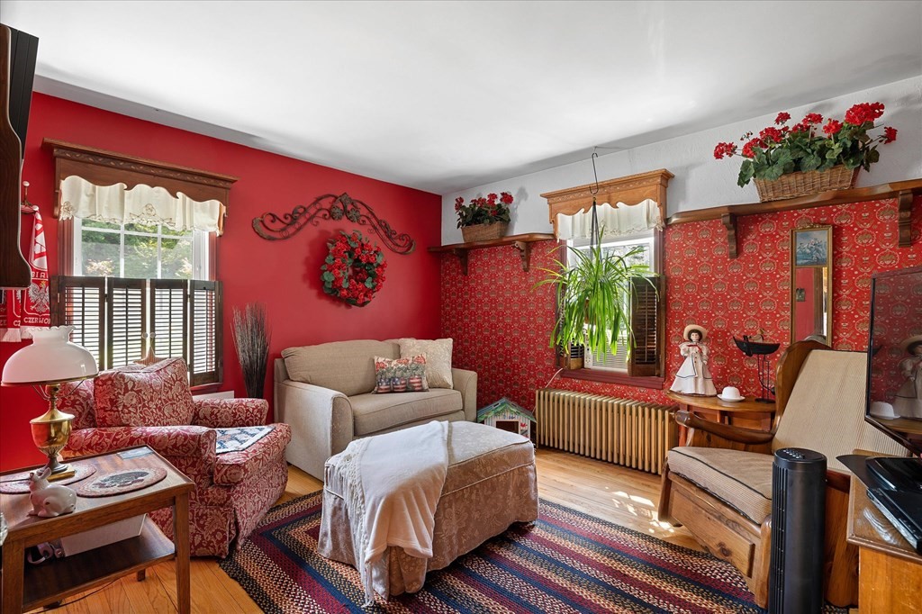 Living room with red walls, patterned wallpaper, floral seating, a beige sofa, and a colorful rug.