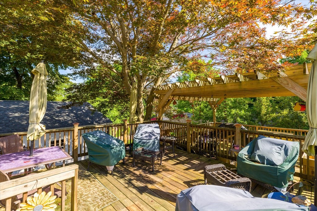 Wooden deck with cushioned patio seating beneath a pergola and colorful autumn foliage.