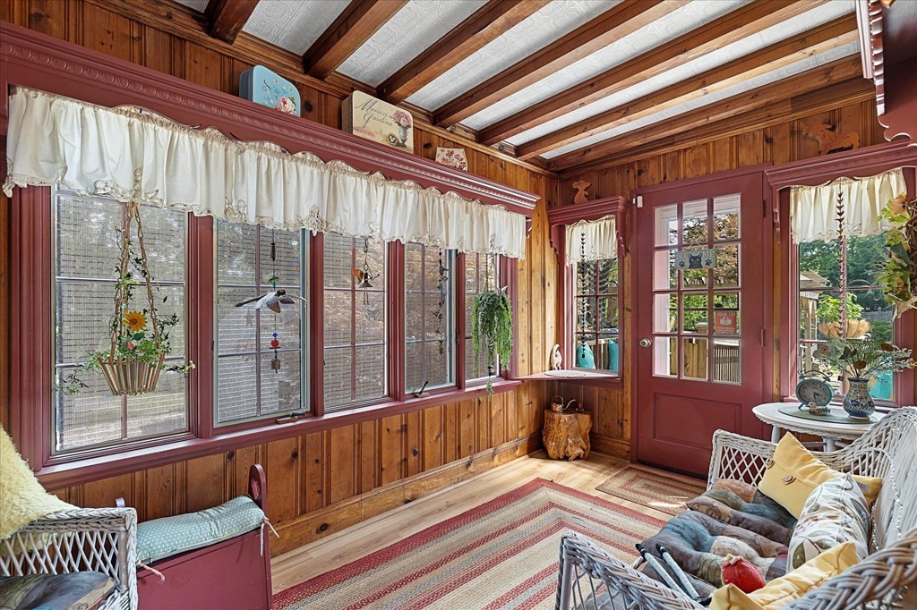 Sunroom with wood-paneled walls, exposed beams, and a wall of windows.