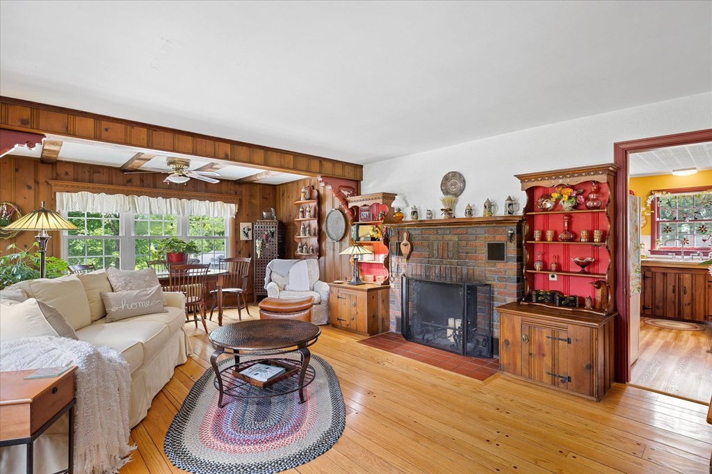 Living room with a stone fireplace, wood-paneled walls, hardwood floors, and an adjoining dining area.
