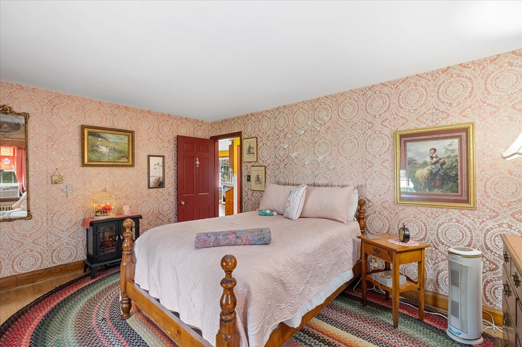 Bedroom with a wooden four-poster bed, ornate pink wallpaper, and a colorful patterned rug.