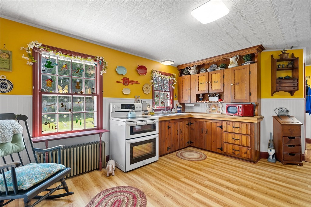 Kitchen with vintage wooden cabinets, mustard-yellow walls, and a white range beside decorative windows.