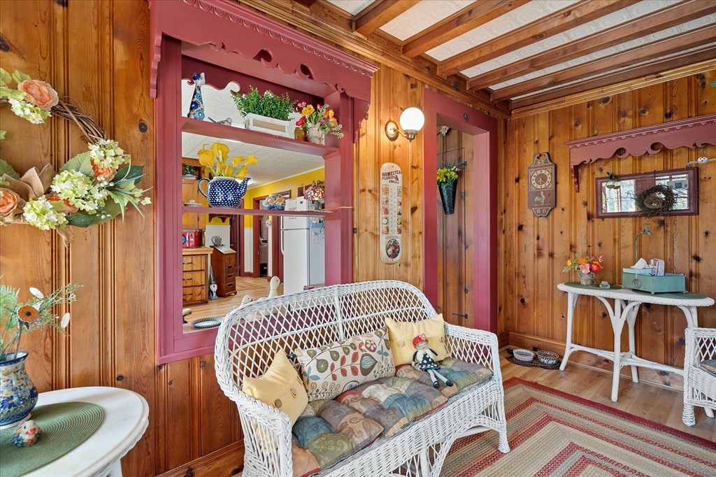 Wood-paneled sitting room with a white wicker loveseat and a kitchen visible through a red-trimmed pass-through.