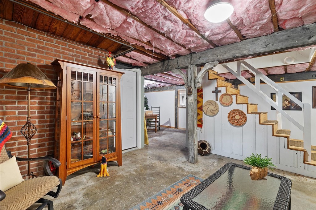 Furnished basement with exposed brick walls, ceiling beams, and a wooden display cabinet.