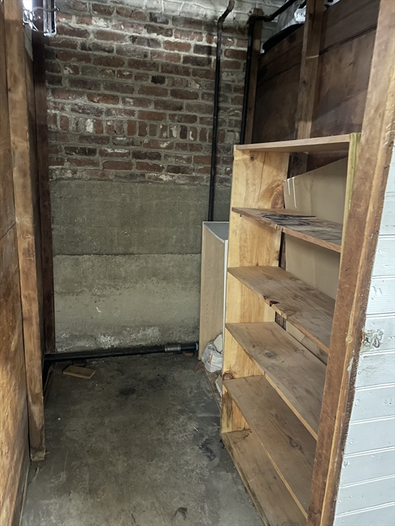 Unfinished basement storage area with rough wooden shelving and exposed brick and concrete walls.