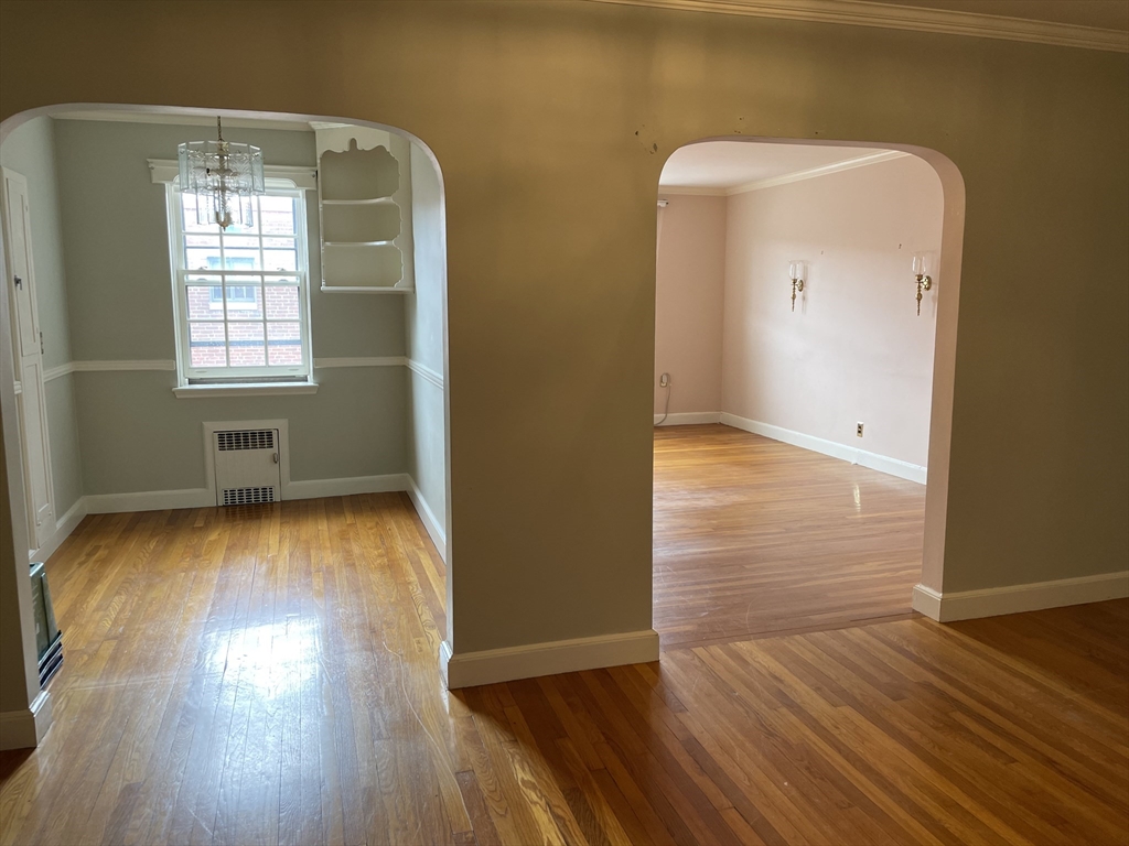 Vacant rooms with hardwood floors, arched openings, built-in shelves, and a large window.
