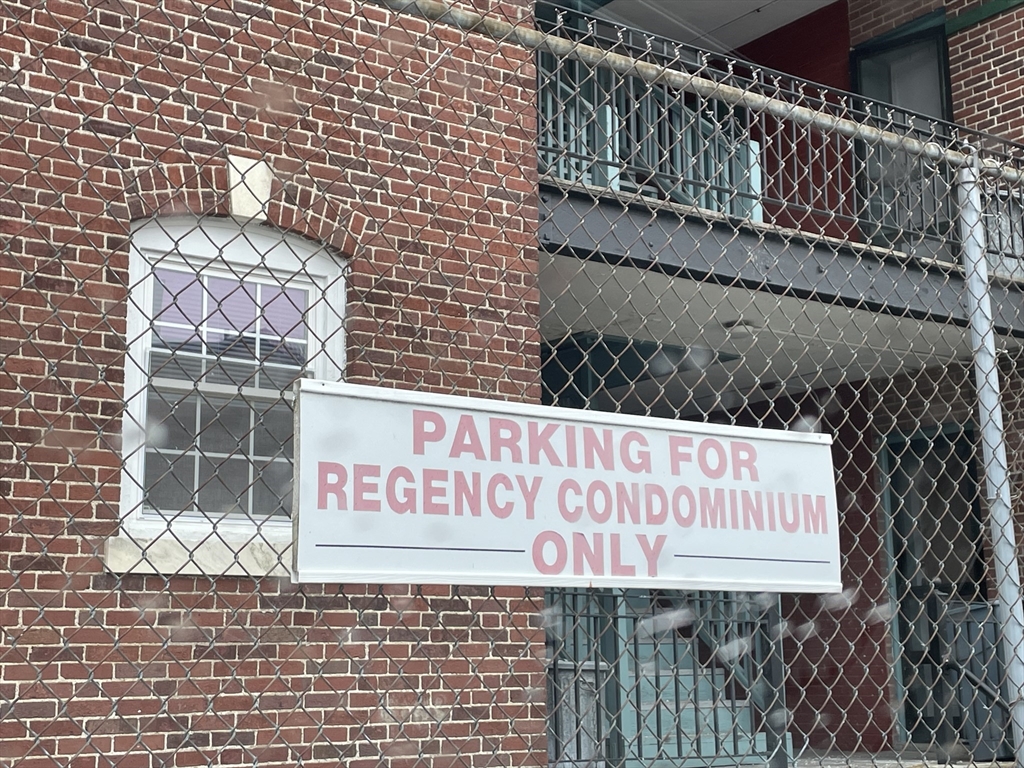 Brick condominium facade behind chain-link fencing, with a sign reserving parking for Regency Condominium.