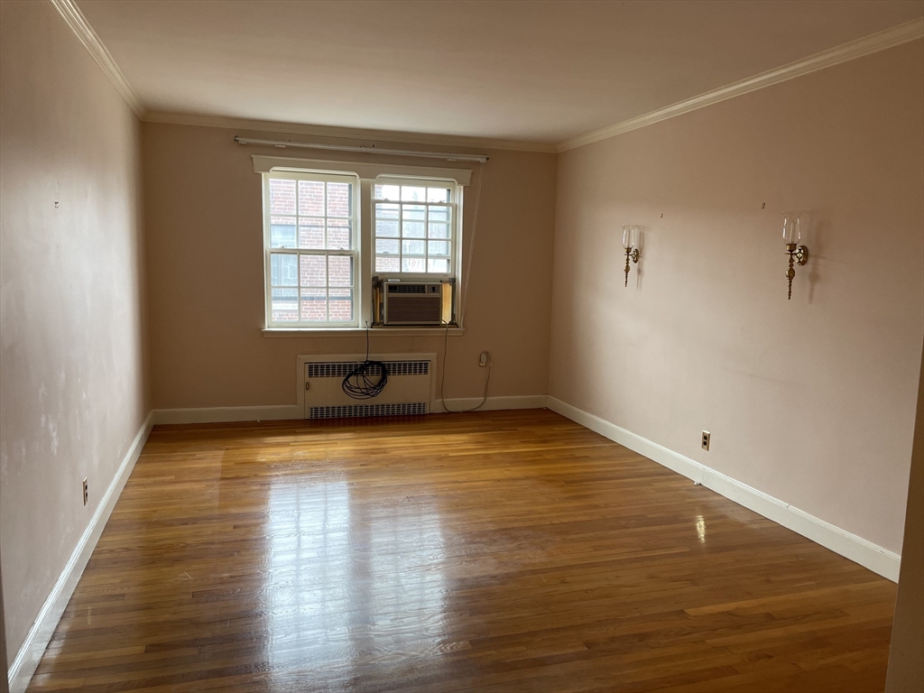 Empty room with polished hardwood floors, two windows, and a window air conditioner.