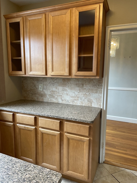 Kitchen with honey-colored cabinets, granite counter, and tile backsplash beside an open doorway.