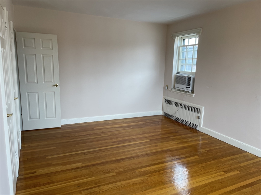 Empty room with polished hardwood floors, a window air conditioner, and radiator cover.