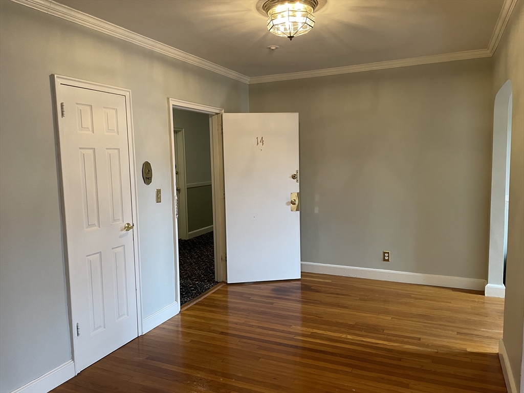 Empty room with polished hardwood floors, crown molding, and an open door marked 14.