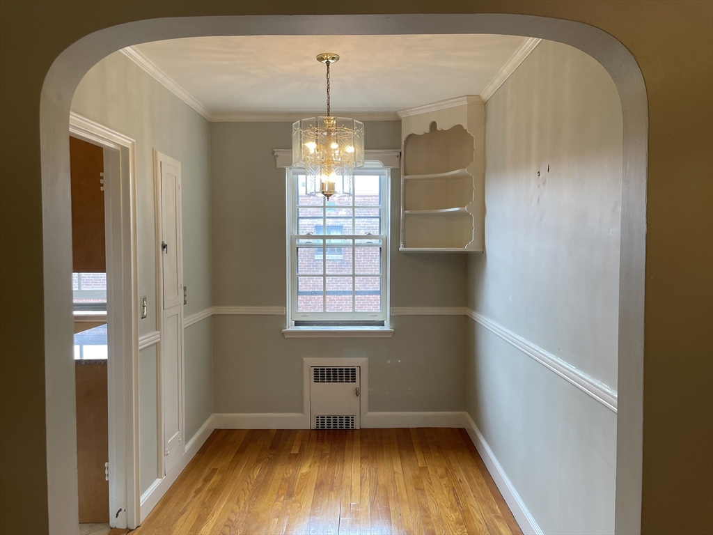 Empty dining room with hardwood floors, a chandelier, and built-in shelves beside the window.