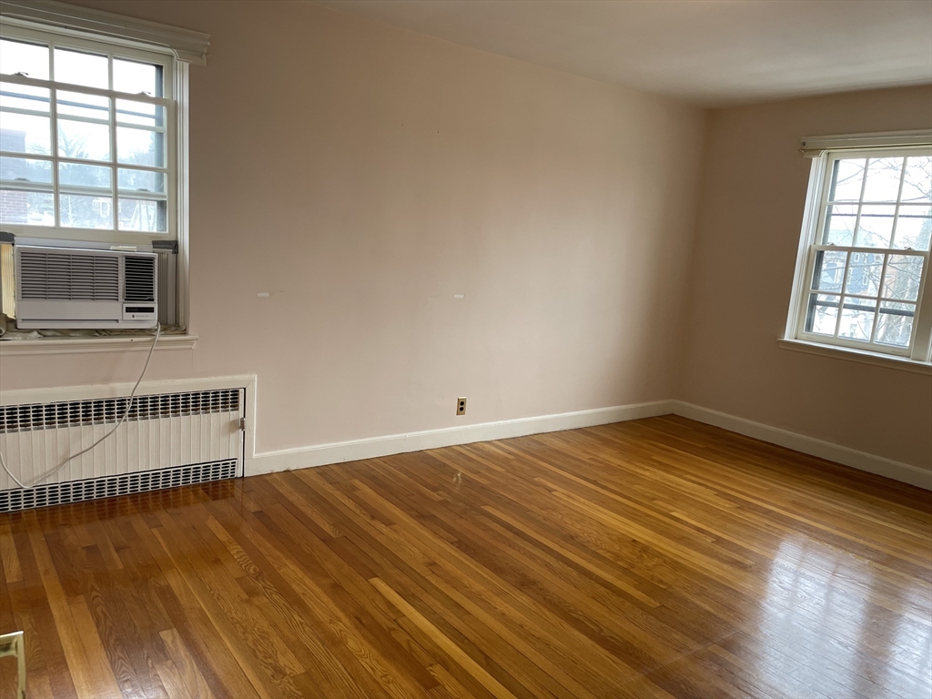 Empty room with polished hardwood floors, two windows, and a window air conditioner.