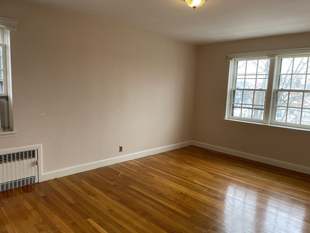 Empty room with polished hardwood floors, a radiator, and large windows.