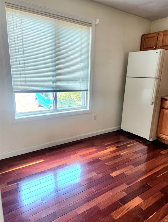 Kitchen corner with a white refrigerator, wooden cabinets, and sunlit hardwood floors.