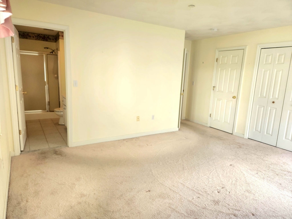 Empty carpeted bedroom with white closet doors and an open doorway to a bathroom.