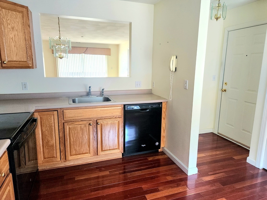 Kitchen with oak cabinets, a black dishwasher, and dark hardwood floors.