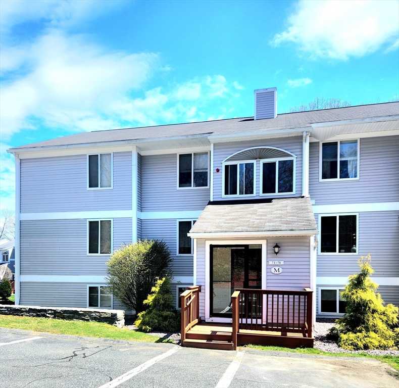 Gray-sided residential building with a covered entrance and wooden deck.