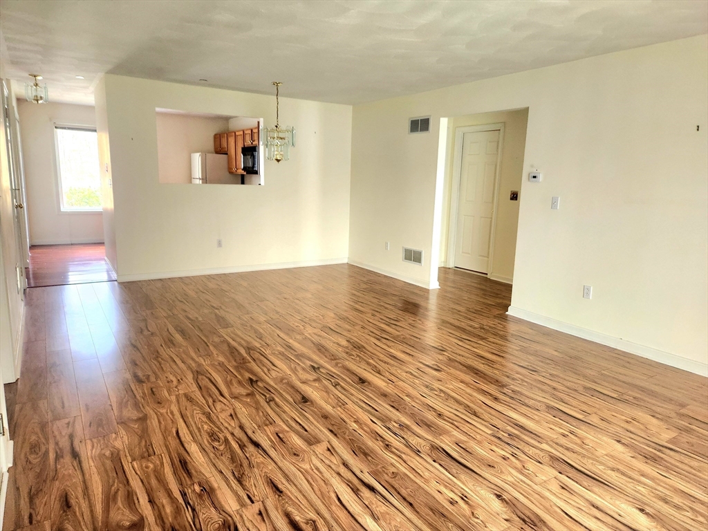 Unfurnished living and dining area with wood-look floors and a pass-through to the kitchen.