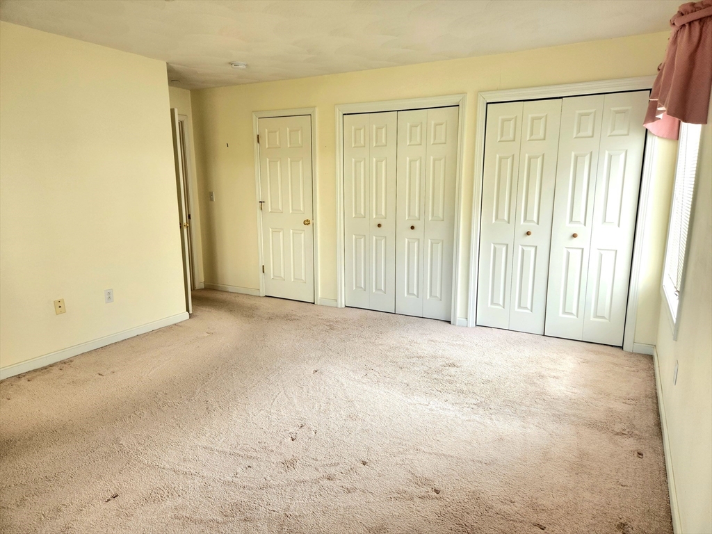 Empty bedroom with worn beige carpet, white closet doors, and a window.