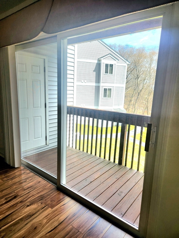 Sliding glass door opens onto a wood-plank balcony overlooking a neighboring apartment building.