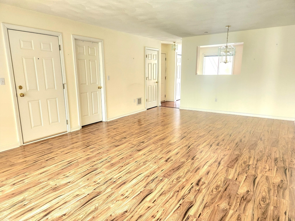 Empty living and dining area with hardwood floors and a chandelier beyond the wall opening.