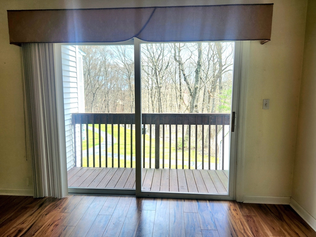 Empty room with wood-look flooring and a sliding glass door to a balcony overlooking trees.