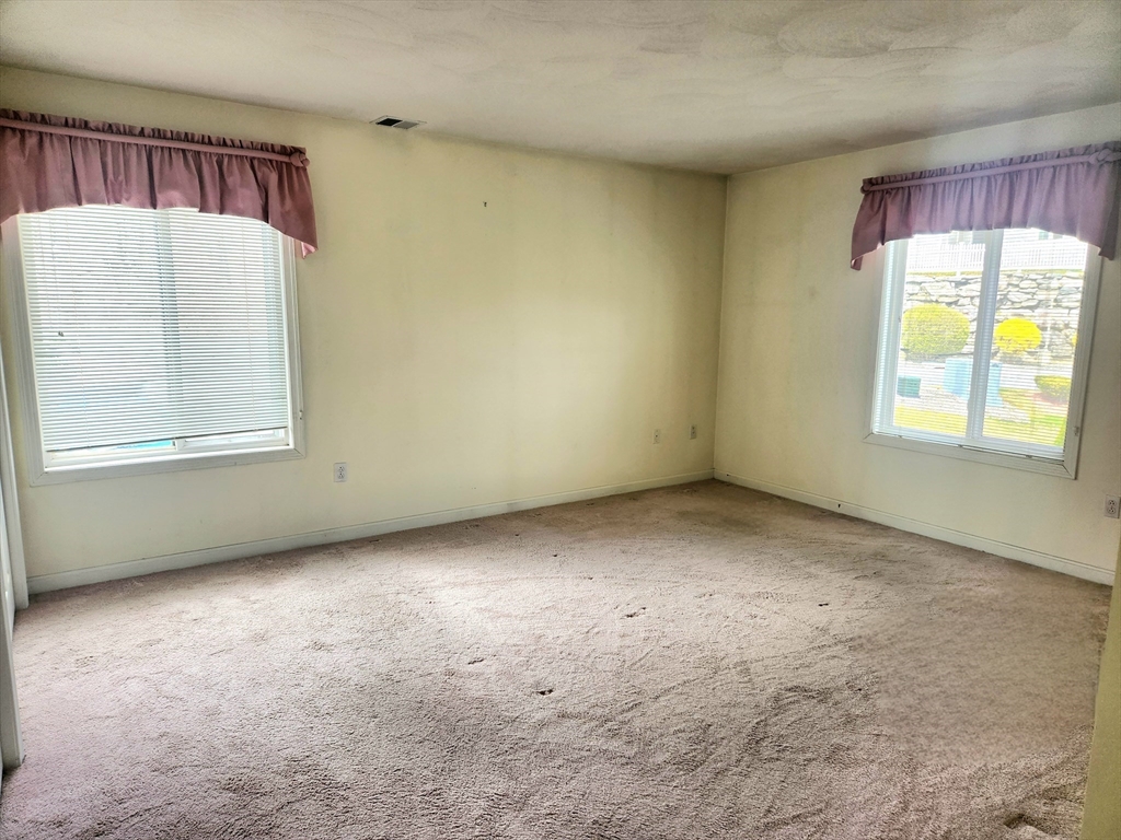 Vacant carpeted room with two windows, blinds, and mauve valances.