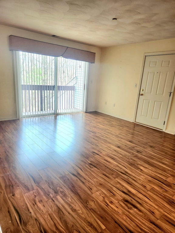 Empty living room with wood-look flooring and a sliding glass door with vertical blinds.
