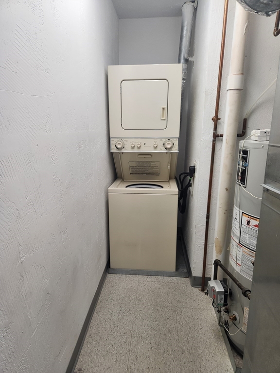 Laundry area with a stacked washer and dryer beside a water heater and exposed pipes.