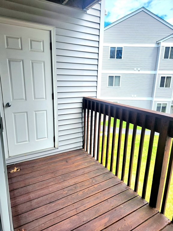 Wooden balcony with dark railing beside a white exterior door, overlooking a neighboring building.