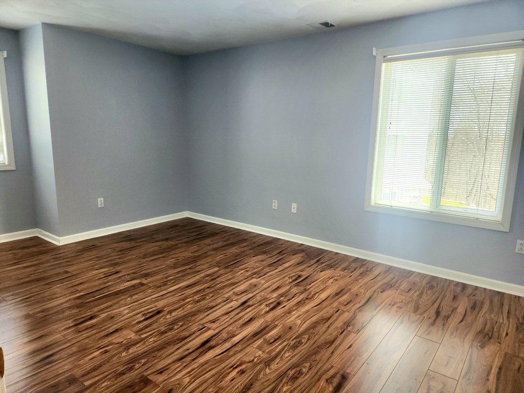 Empty room with gray walls, dark wood-look flooring, and a large window with blinds.