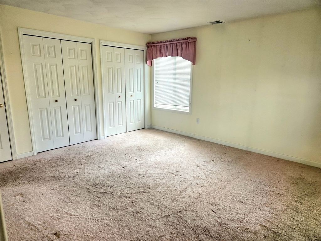 Vacant bedroom with two sets of white closet doors and a window with blinds and a mauve valance.